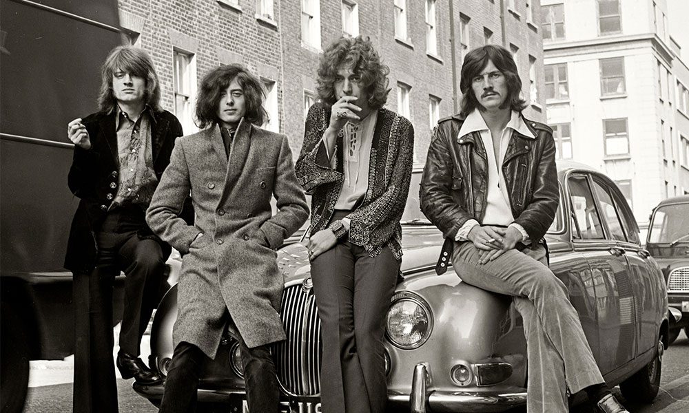 The Led Zeppelin band leaning against a car